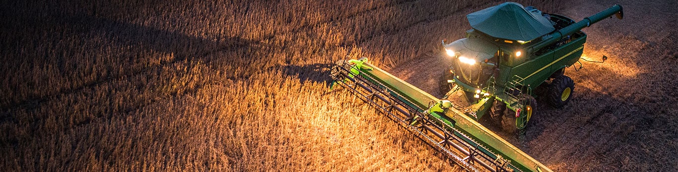 Vista aérea de una cosechadora cosechando soja bajo la luz del crepúsculo, mostrando los patrones de campo texturizados.